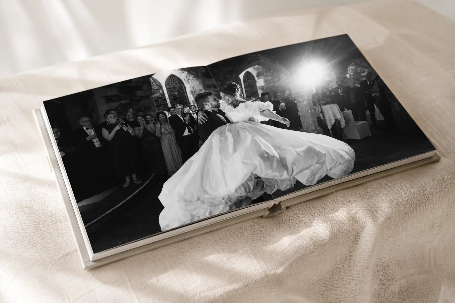 An open wedding album resting on a linen-covered surface, light falling across the lay-flat pages.